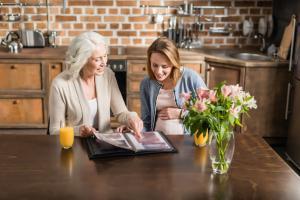 Young pregnant woman looking at photo album with senior woman, both smiling