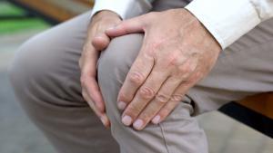 Close-up of man's hands massaging his own knee through pants