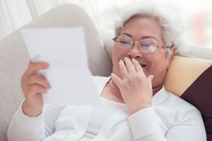 Senior woman recling on couch, smiling as she reads letter