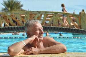 Senior man smiling, leaning over the edge of a pool