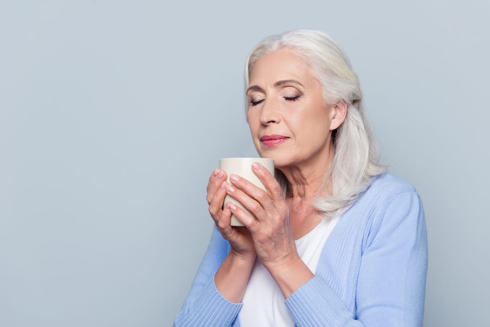 Senior woman smelling cup of coffee, smiling