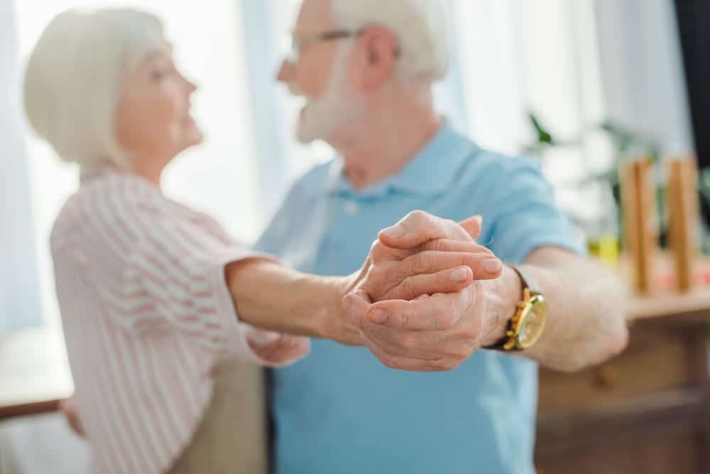 Focus on the hands of a senior couple dancing inside