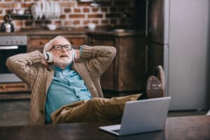 old man sitting in chair listening to headphones, leaning back, smiling