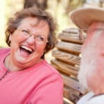 Senior woman laughing outside on bench, senior man in foreground blurry