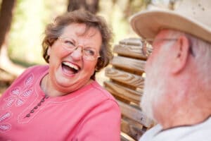 Senior woman laughing outside on bench, senior man in foreground blurry