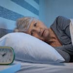 Senior woman lying awake in bed, distressed, insomnia
