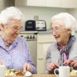Two smiling senior women eating together at table