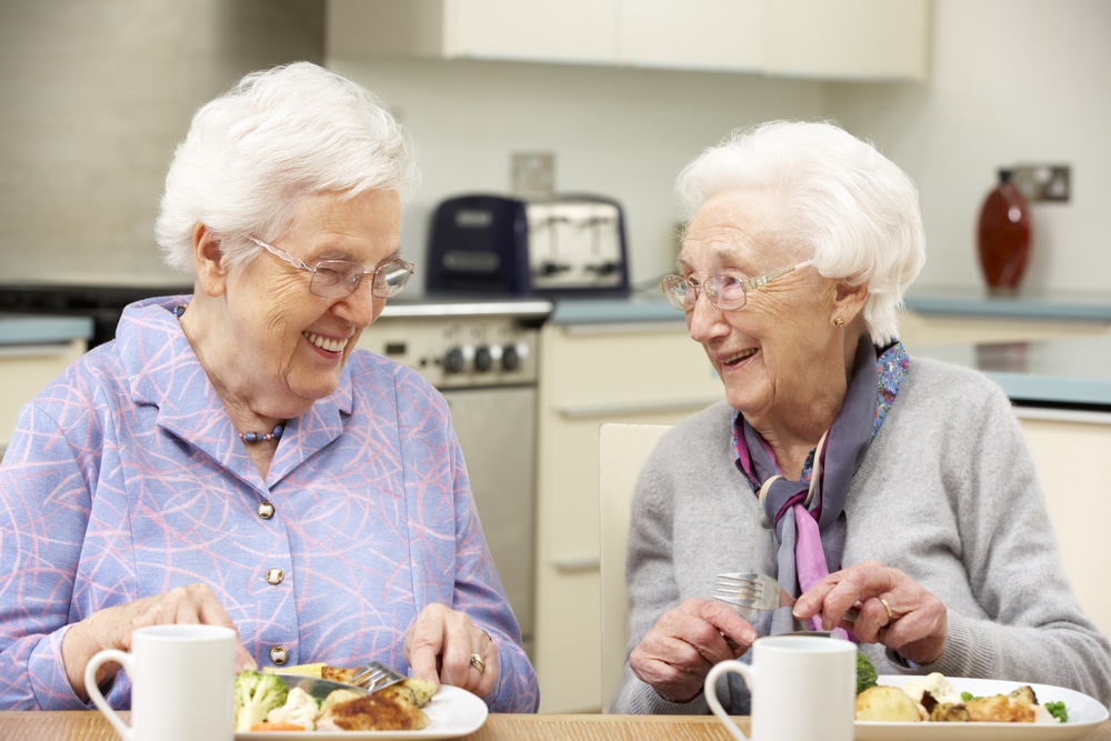 Two smiling senior women eating together at table