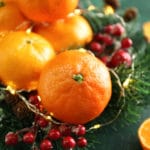clementines surrounded by lights, garland, and cranberries