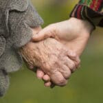 Senior holding younger person's hand outdoors