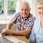 Two smiling seniors using laptop together