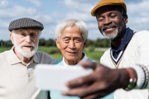 Three senior men smiling at phone for selfie while golfing