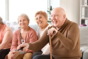 three smiling seniors hanging out, one using tv remote