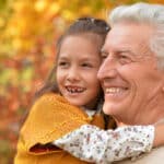senior man with smiling granddaughter outside in fall