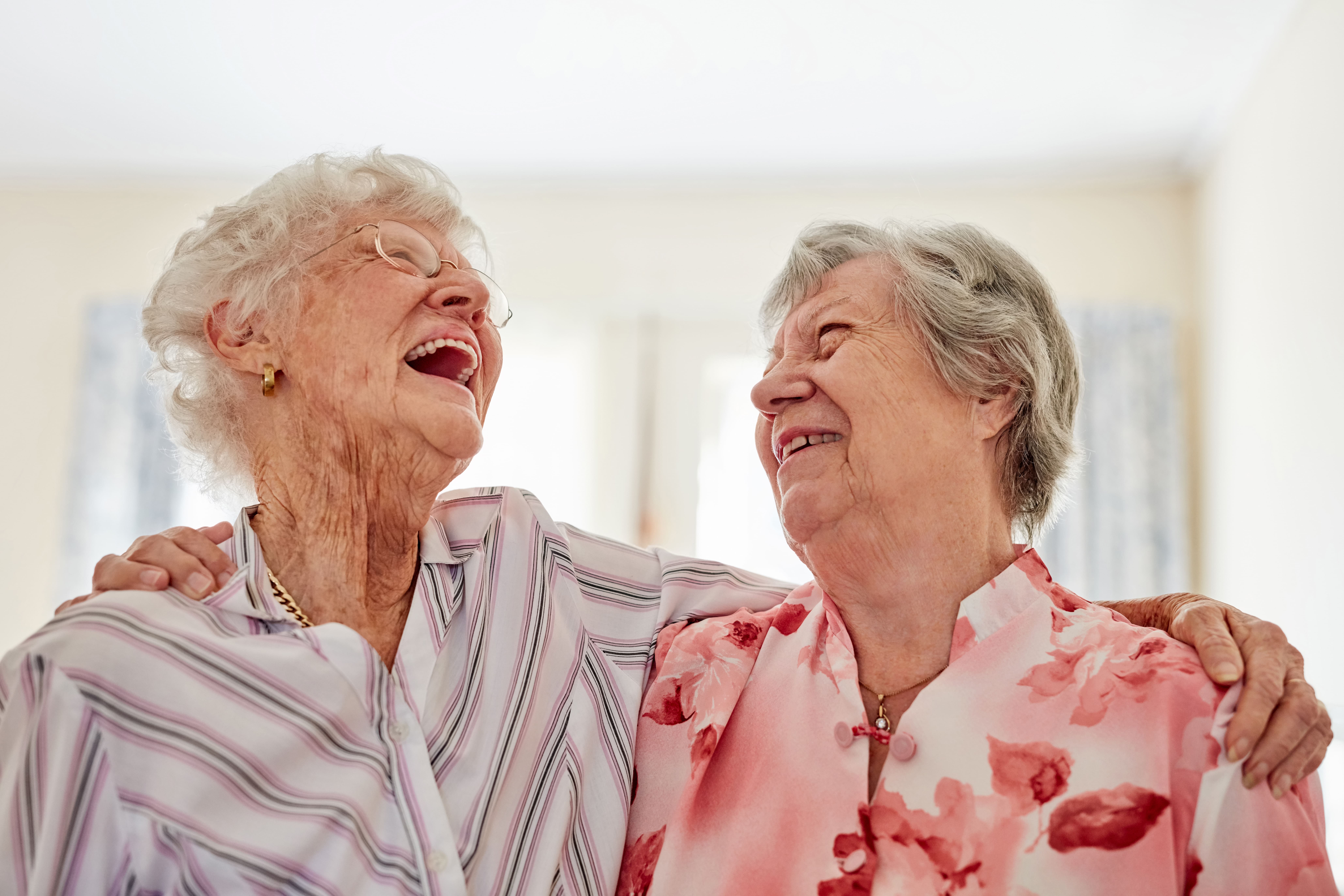 two senior women, arms around each others shoulders, laughing