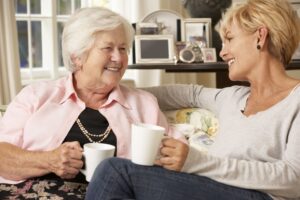 Adult woman and senior woman enjoying a cup of coffee and laughing at home