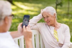 Senior man taking photo of senior woman on bench in park